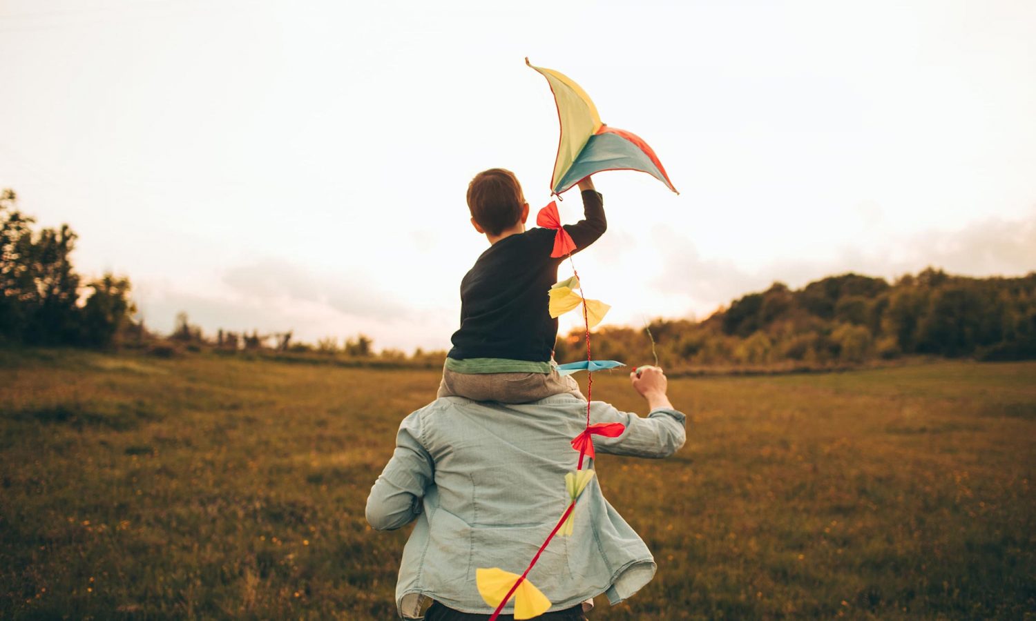 A child with a kite on his father's shoulders