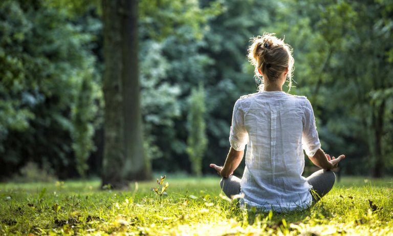 A woman sitting cross-legged on the grass while meditating.