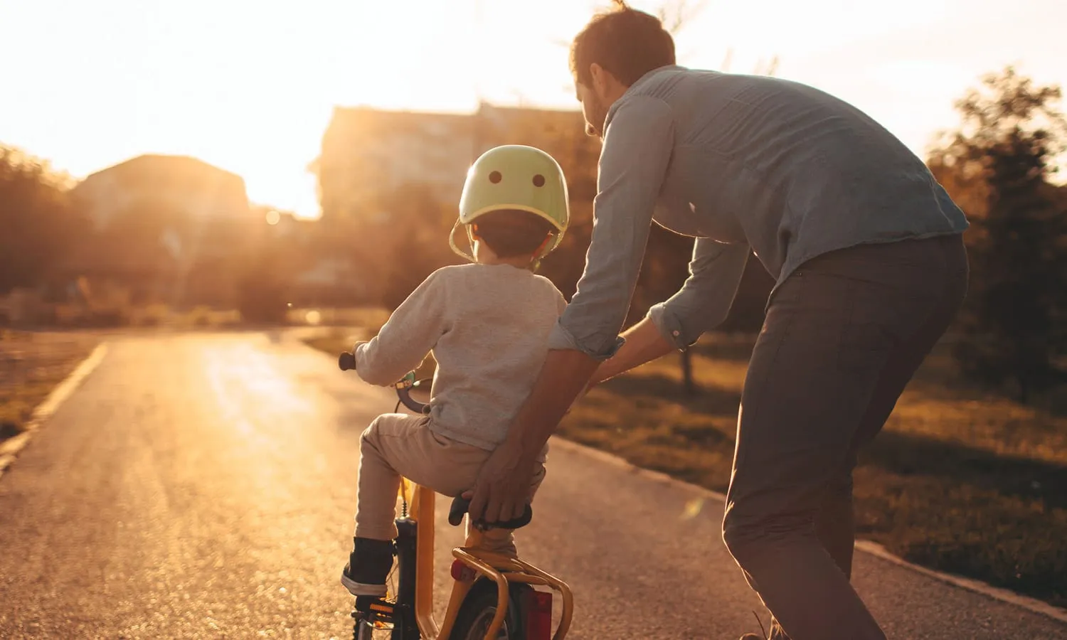 Man riding a bike with a child on the back, sunset.