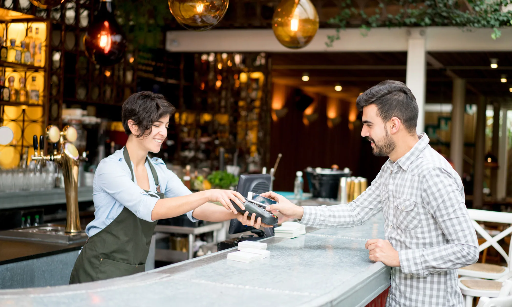 A man and a woman in a restaurant, the man is taking payment from a woman who has her wallet out.