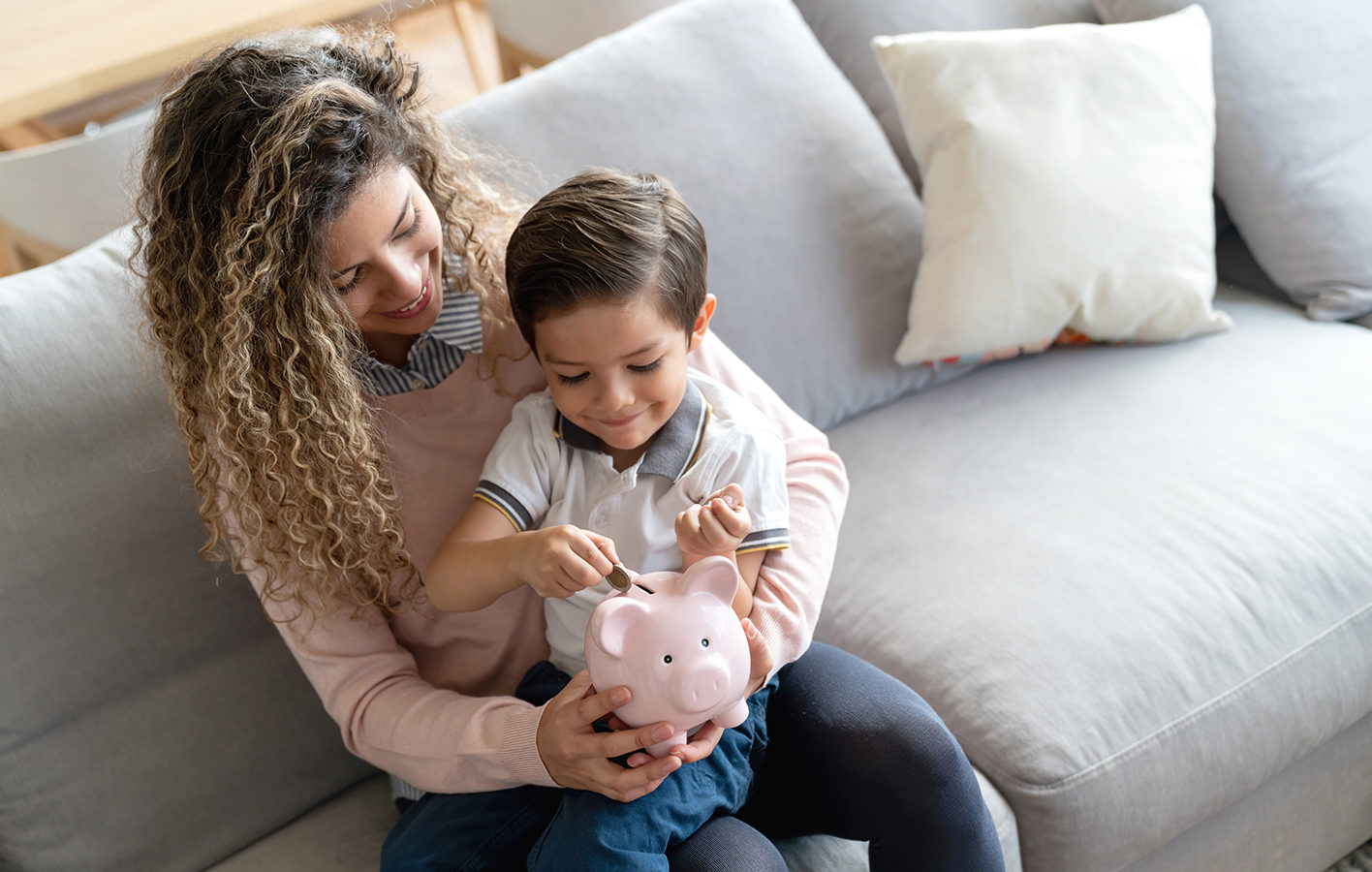 A woman and a child sitting on a couch with a piggy bank in their hands.