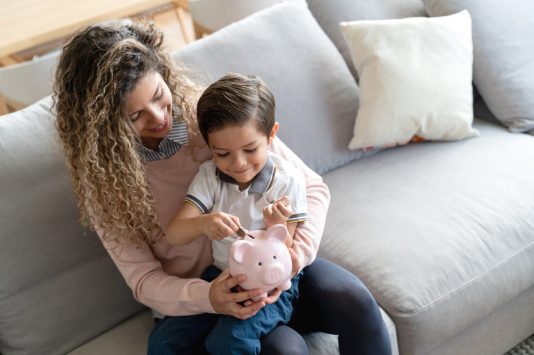 A woman and a child sitting on a couch with a piggy bank in their hands.