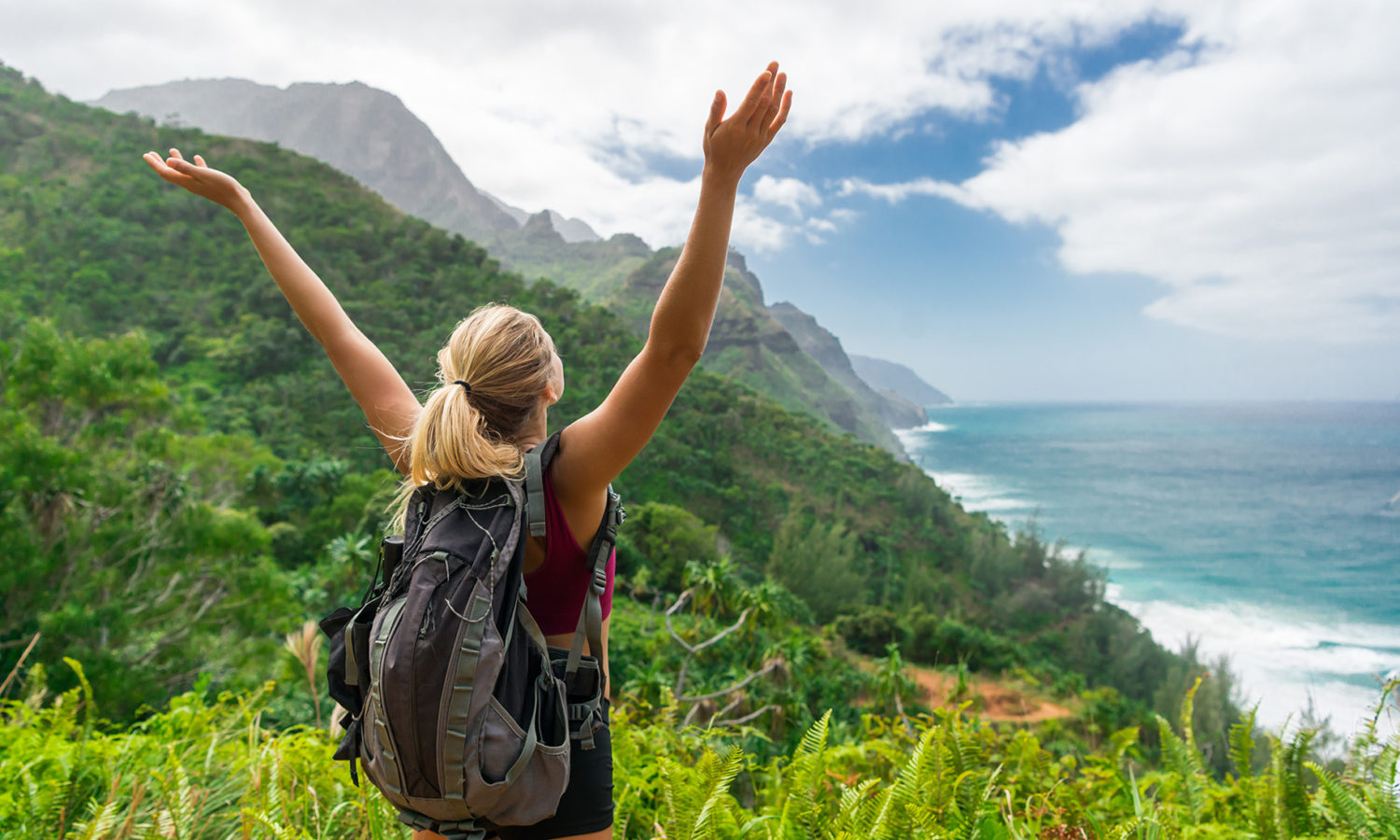 Woman on a hike in nature, celebrating her accomplishment with her arms raised high.