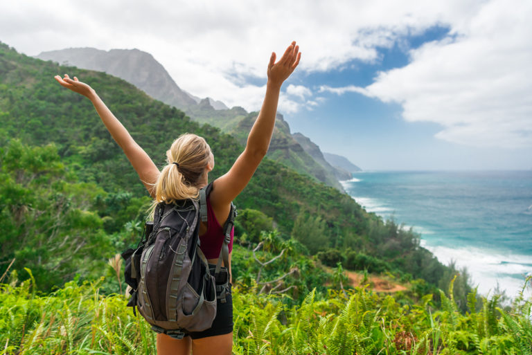 Woman on a hike in nature, celebrating her accomplishment with her arms raised high.