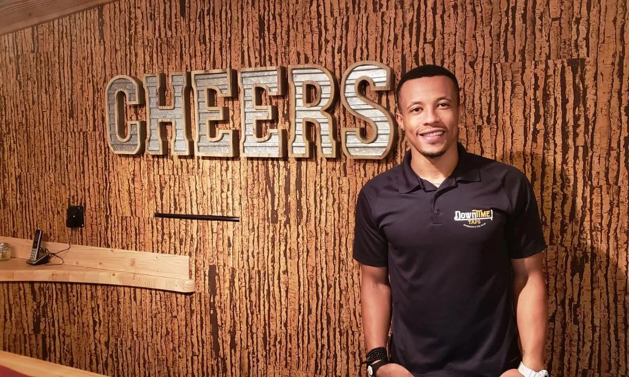 Man standing in front of a wall with the word 'cheers' on it.
