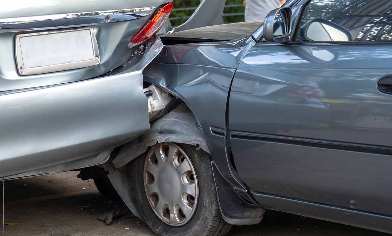 A gray car with a dented hood, parked next to another vehicle in an outdoor parking lot.
