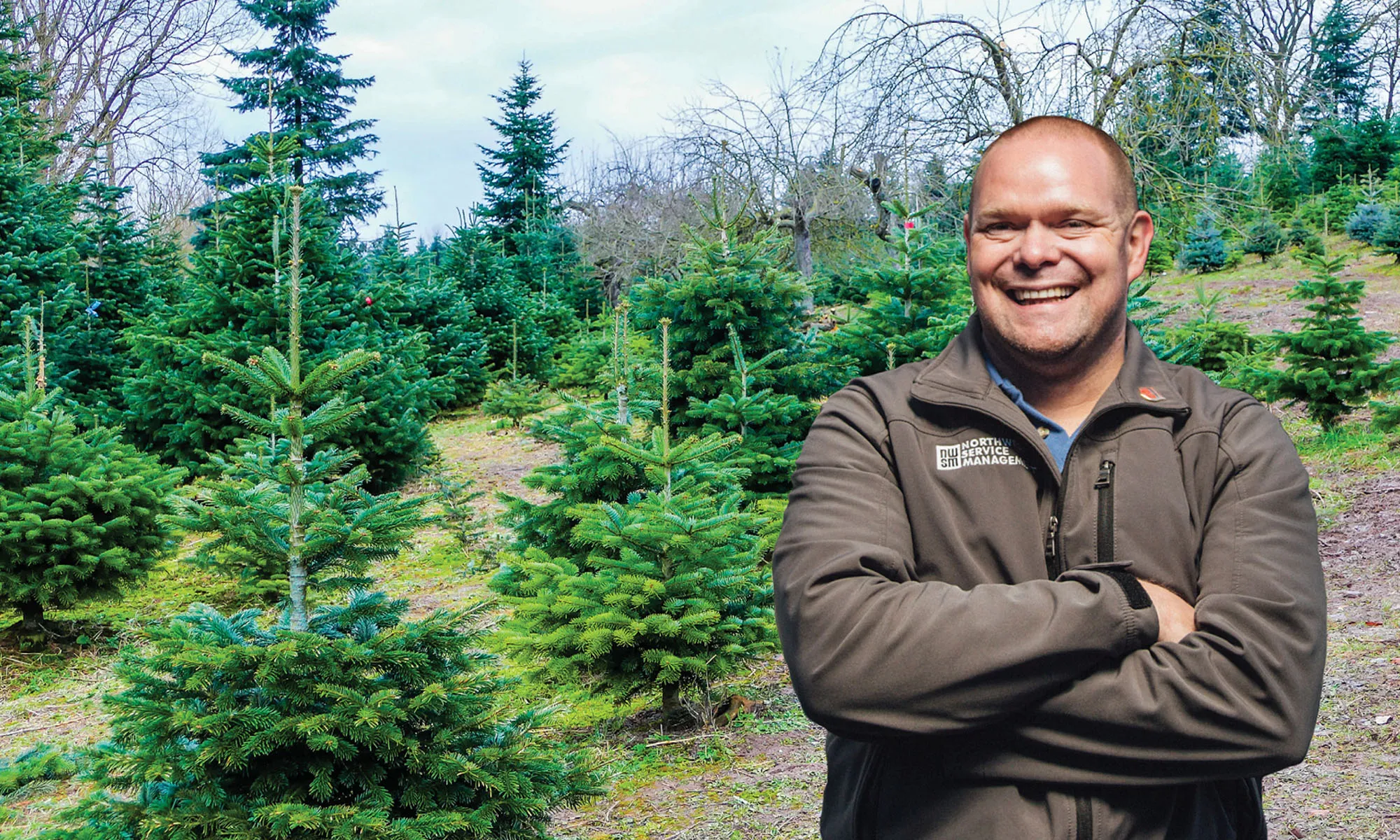 A man standing in front of a field with rows of green trees.