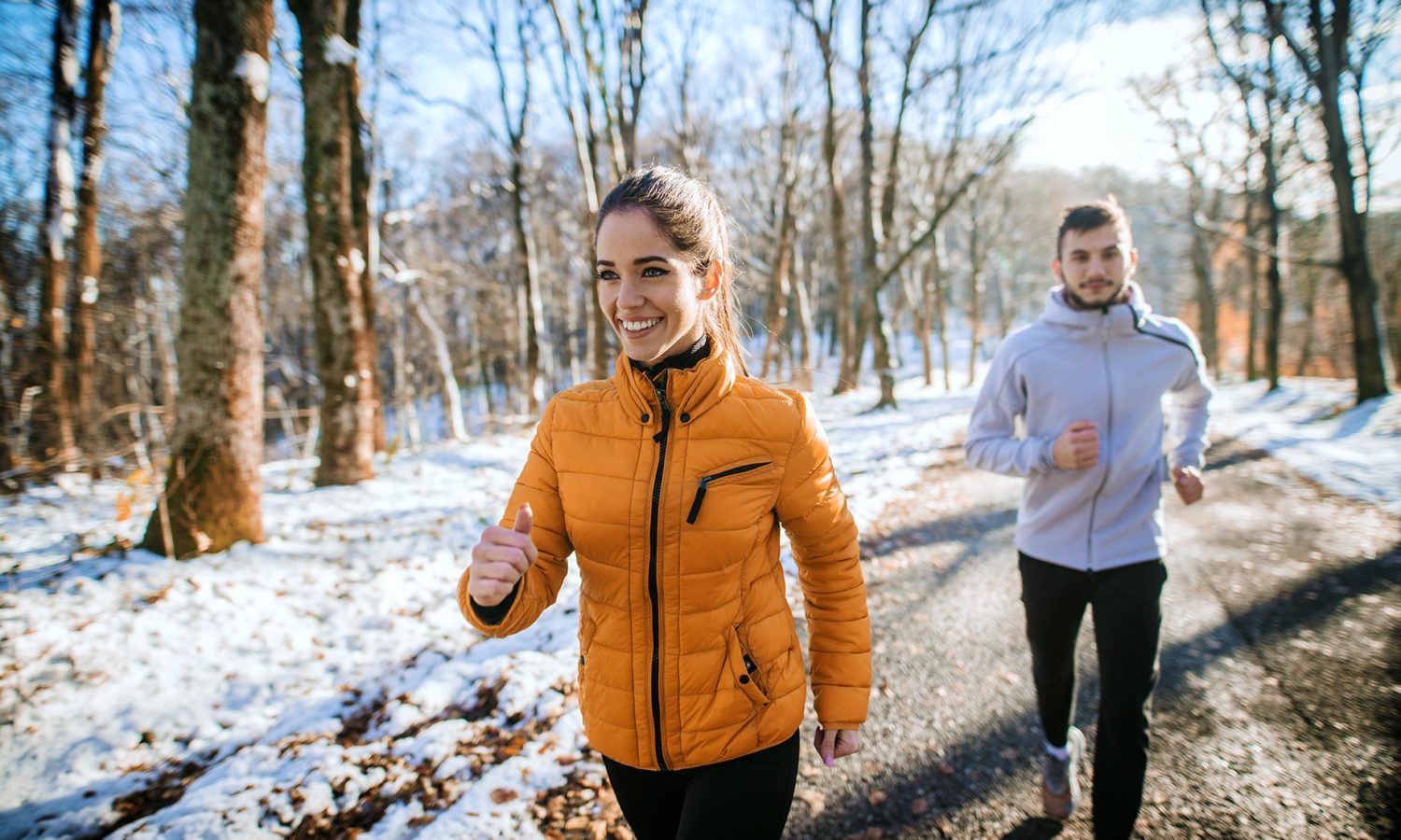 A woman and man jog down a snowy road.