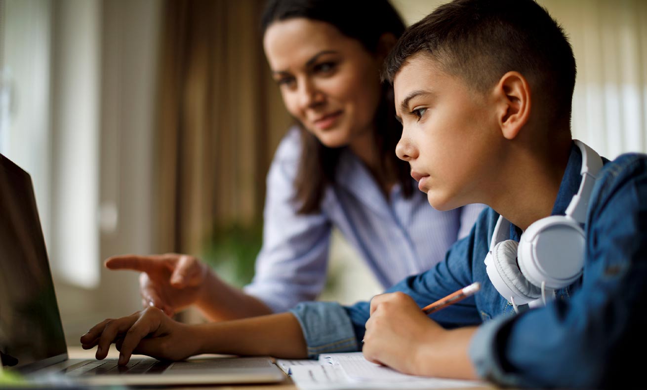 A boy receives financial guidance while working with his mother at a laptop.