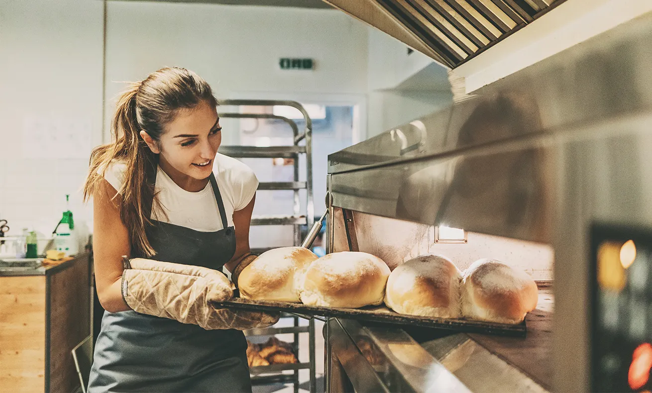 A baker pulls her fresh bread out of the oven.