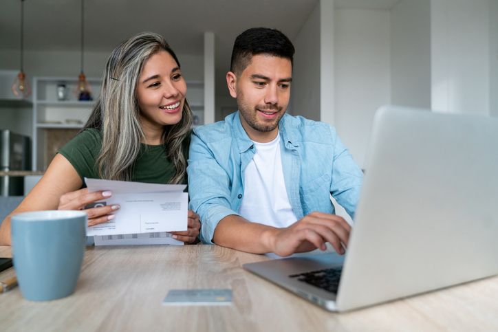 A man and a woman sharing a laptop on a dining table.