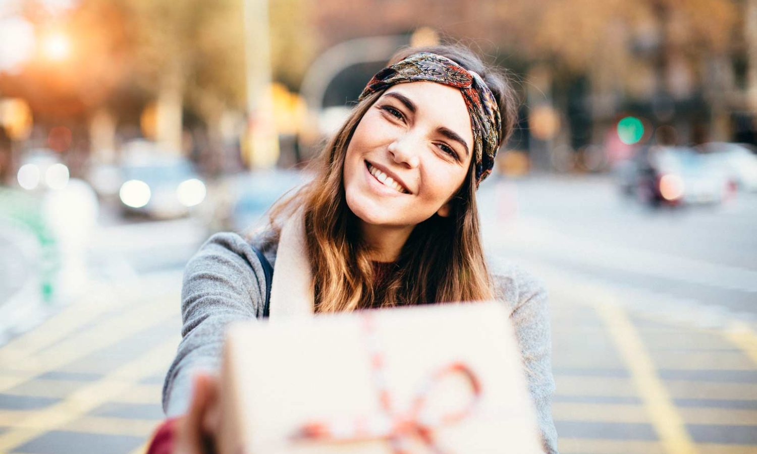 A woman smiles as she hands over a gift wrapped with a bow.