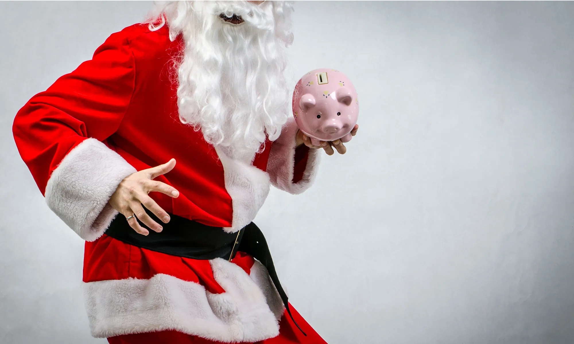 A person dressed in Santa Claus costume holding a piggy bank