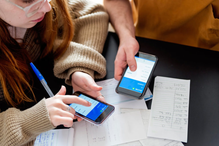 A couple engrossed in their phones, surrounded by papers and a pen.