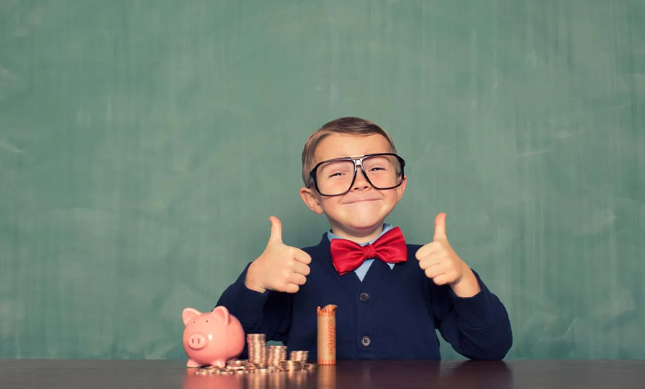 A child giving a thumbs up while posing with play money on a chalkboard background.