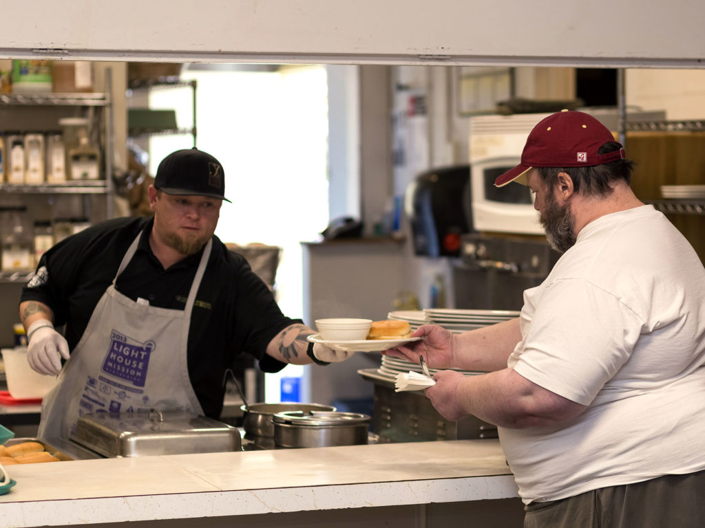 A volunteer at the Lighthouse Mission hands a meal over to a man.