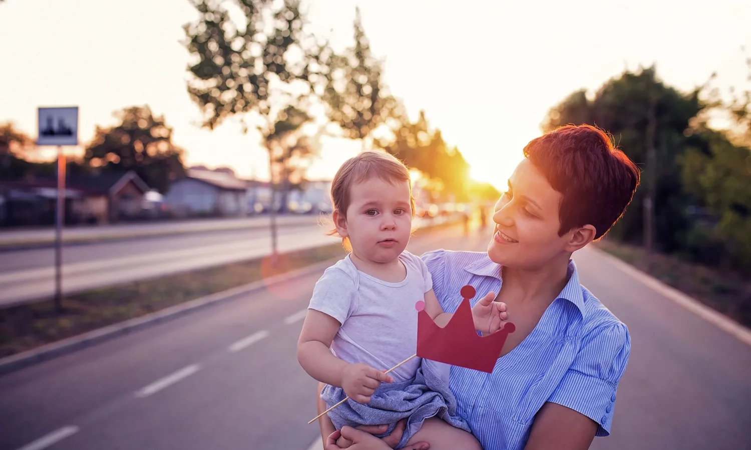 A smiling woman holding a baby while posing in front of a sunset