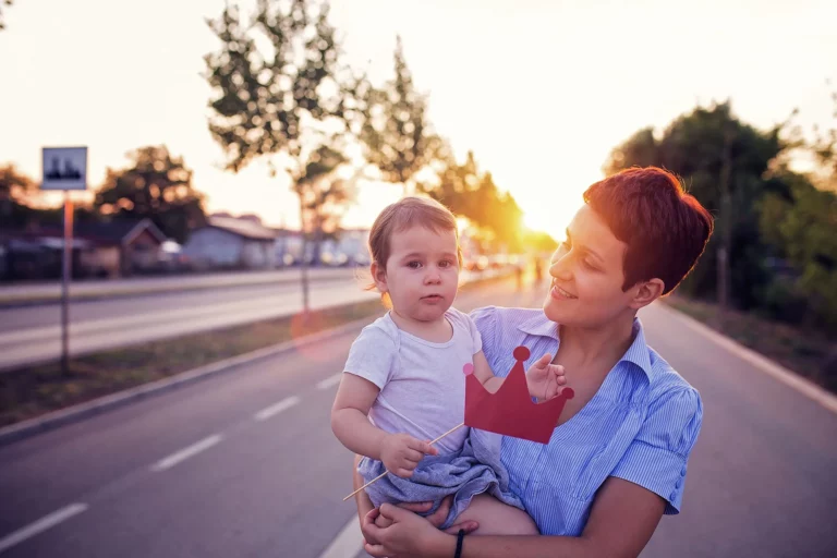 A smiling woman holding a baby while posing in front of a sunset