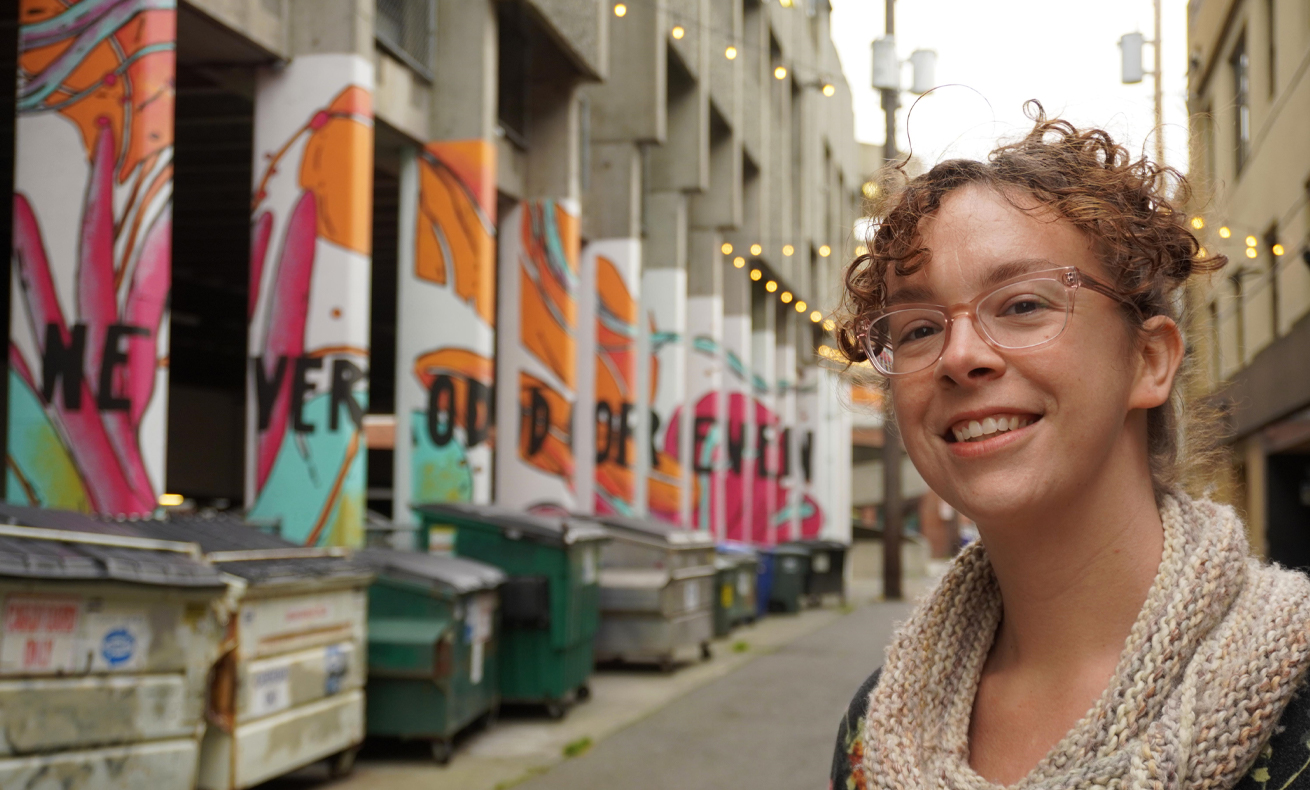 Woman standing on sidewalk in front of large colorful wall.