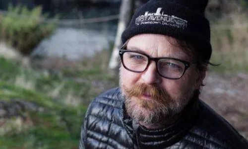Man with beard and glasses in outdoor setting.