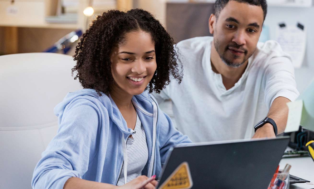 A father helps his daughter with some work on a laptop.