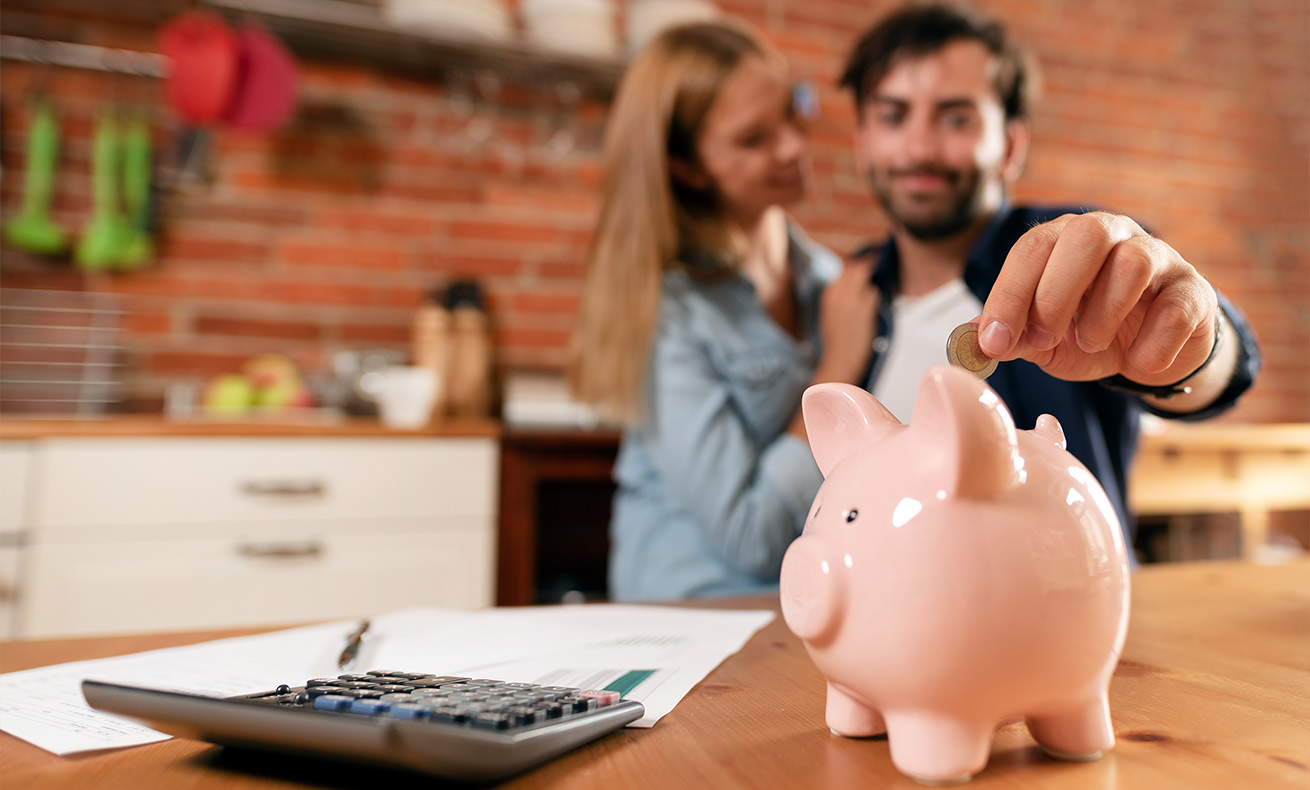 A couple deposits a coin into a piggy bank.