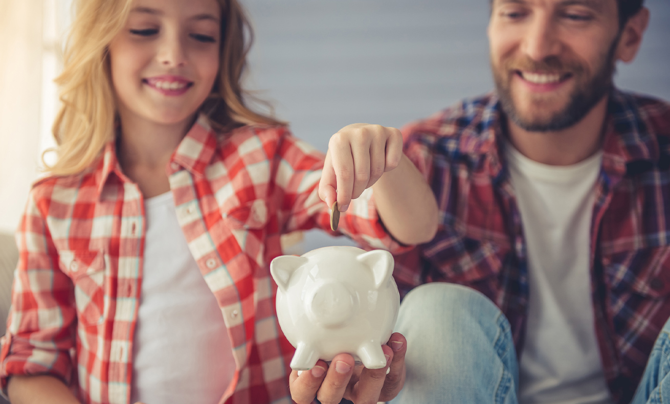 Child reaching for piggy bank with adult supervision.