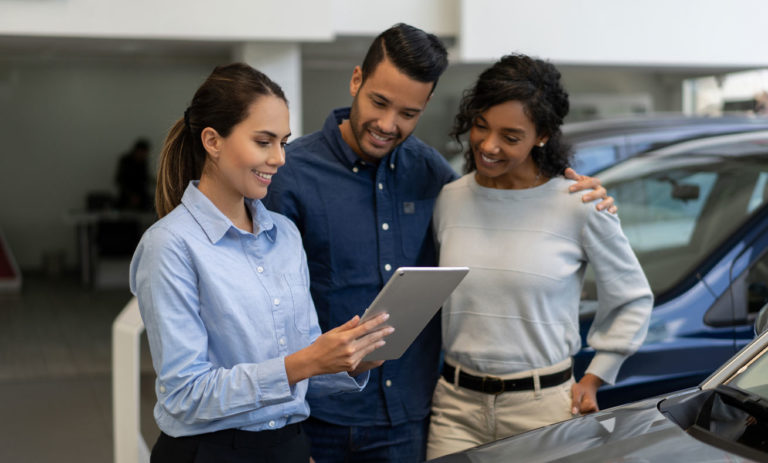 Three people posing in a car showroom with tablet.