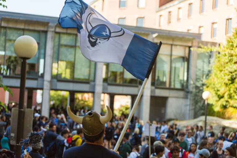 People gathered in an outdoor space, holding a flag with a symbol and a background of buildings.