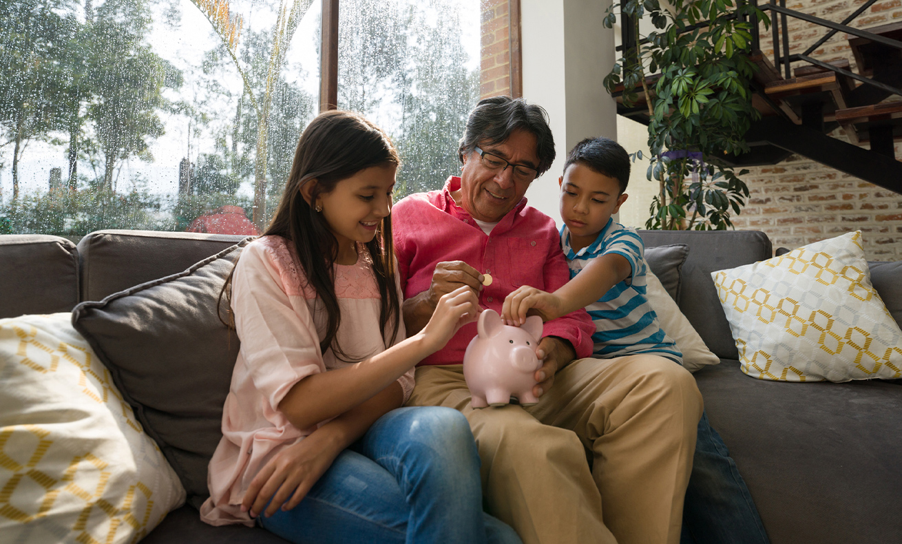 Three people sitting on a couch with a piggy bank in front of them.