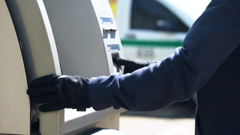 A person in a blue uniform wearing black gloves interacting with an ATM.
