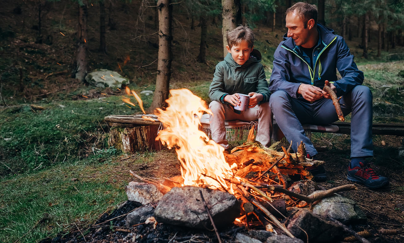 Father and son sit around a campfire.