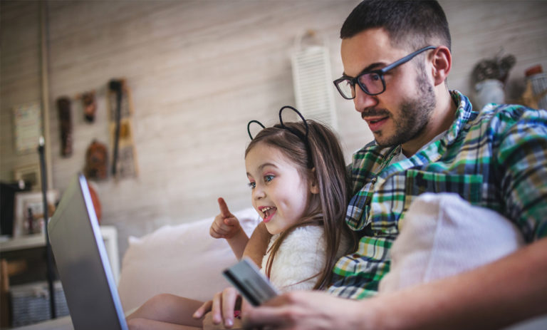 A man and a young girl sitting on the couch, both engaged with their electronic devices.