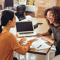 Two women joyfully discuss business loan paperwork sitting between them.