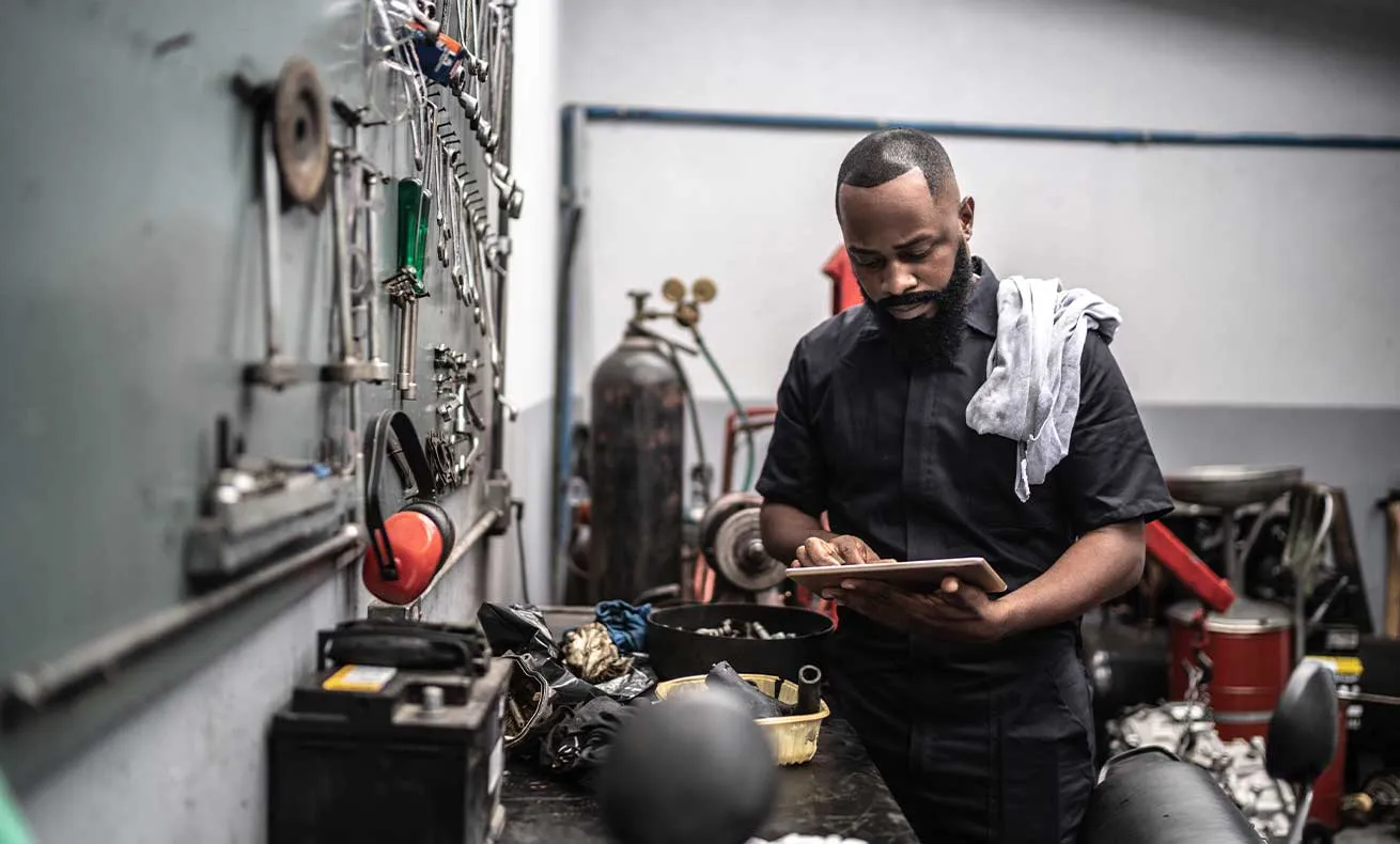A Black man scrolls his tablet in his auto repair shop.