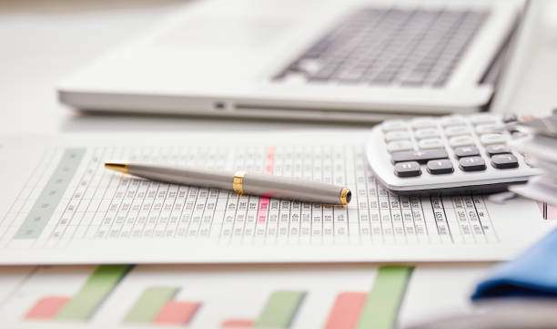 Office desk with laptop, pen and paper, calculator, and financial documents.