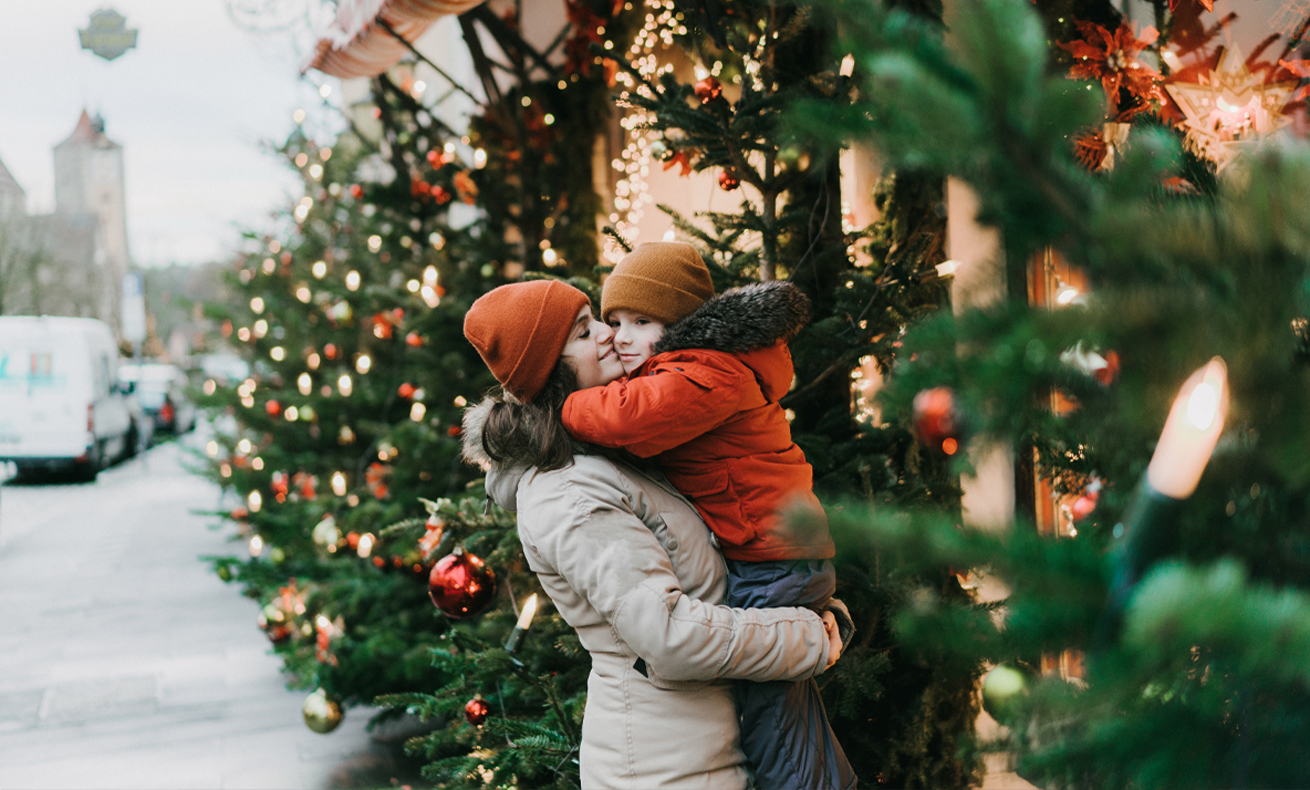 A woman hugging a child near decorated Christmas trees.