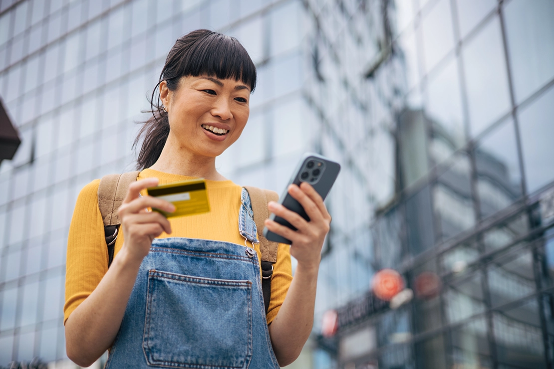 woman with credit card and phone in front of building