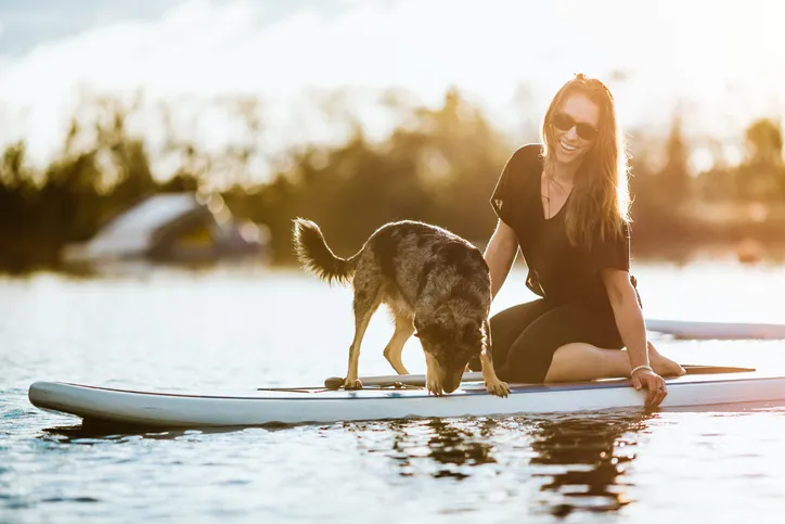 Woman sitting on dock with dog and paddle board.