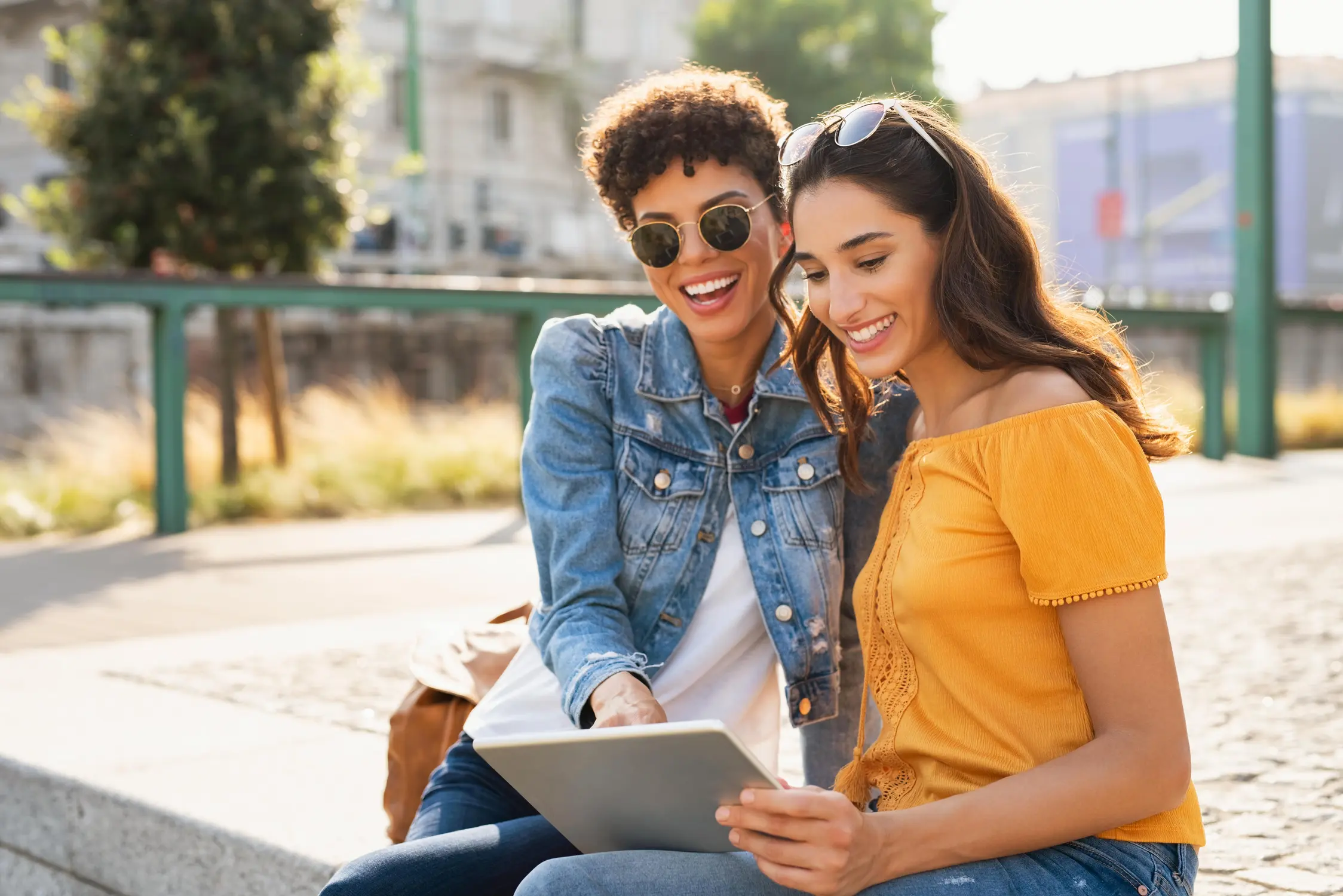 Two women sitting in a park looking at a tablet