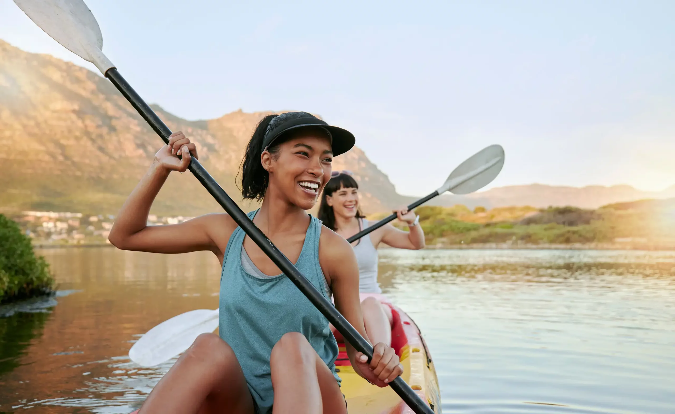 Woman holding kayak paddle, smiling in outdoor setting.