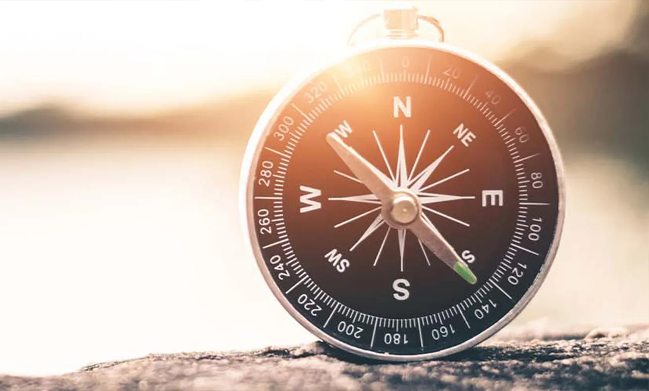 Compass on rock with sunset background.