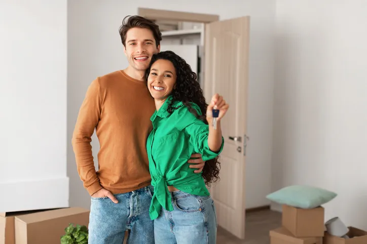 Man and woman posing in front of a house during what appears to be a moving day.