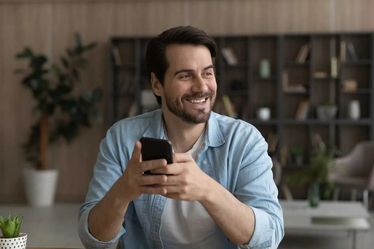 A man smiling and holding a phone.