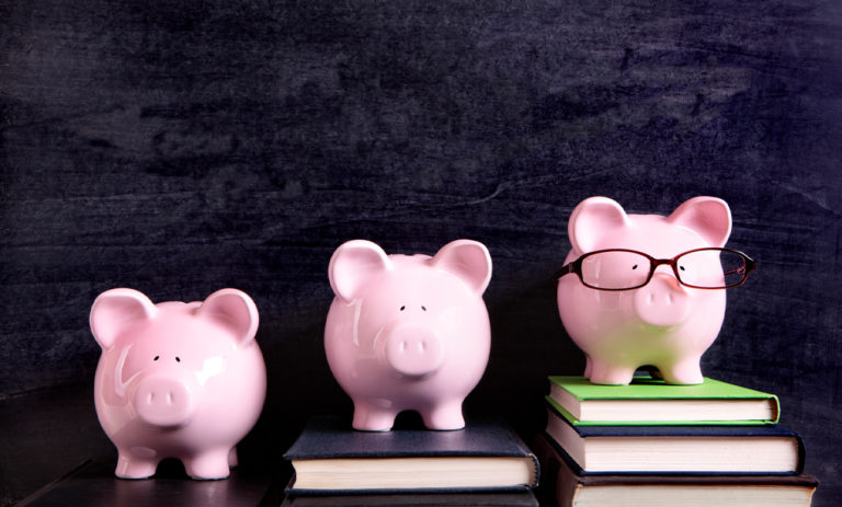 Three pink piggy banks with glasses and a book in the background.