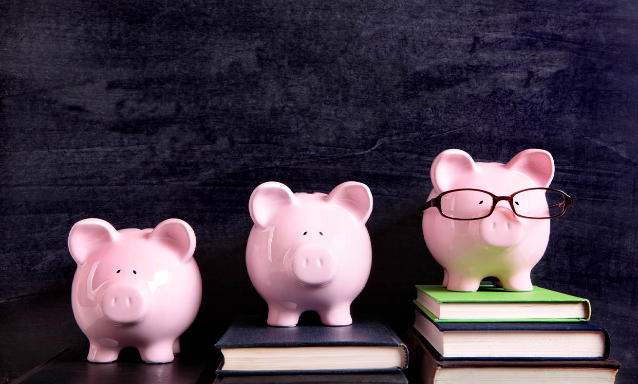 Three pink piggy banks with glasses and a book in the background.