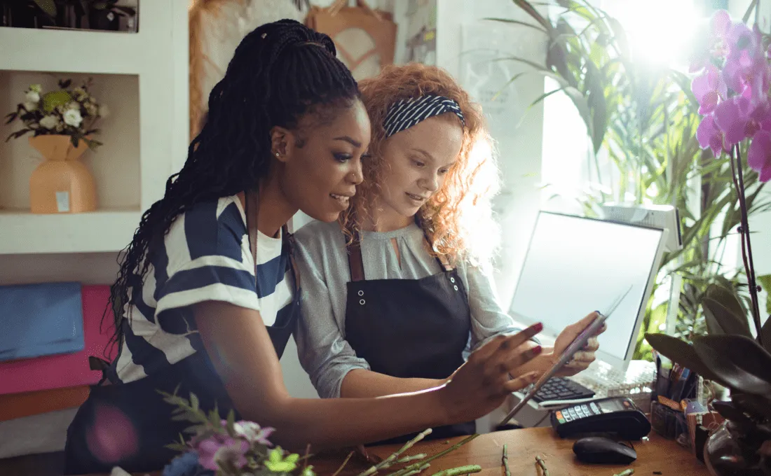 Two women looking at a tablet in a store with plants.