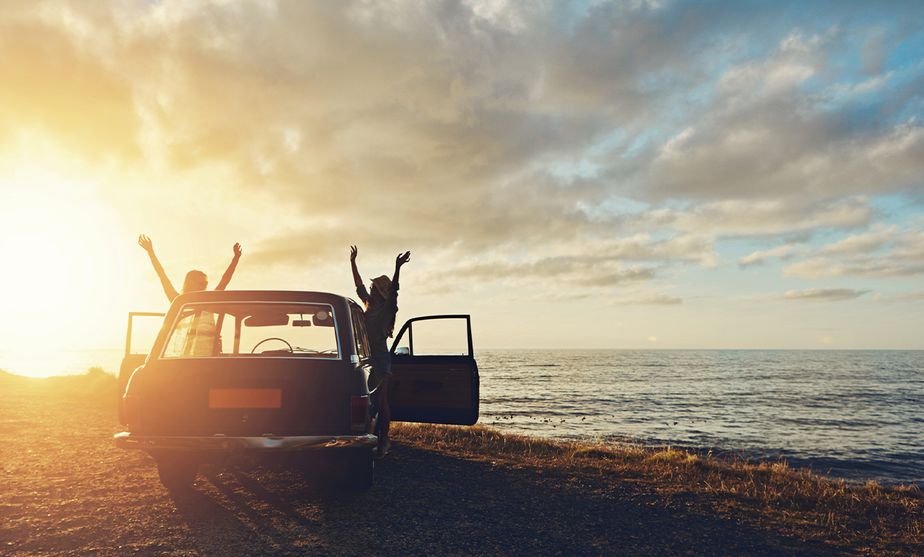 Two people celebrating on beach, car parked nearby.