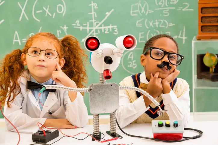 Two children sitting at a desk with a robotic hand.